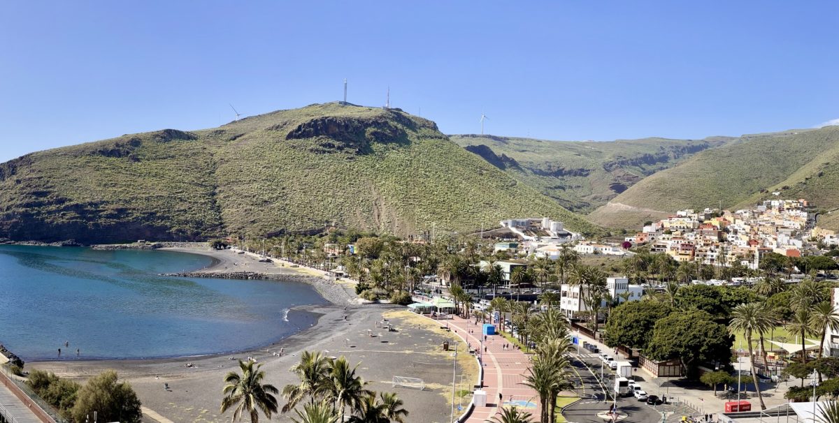 Panoramic view of San Sebastian de La Gomera, with colorful houses and buildings nestled between lush green mountains and the sparkling blue sea.