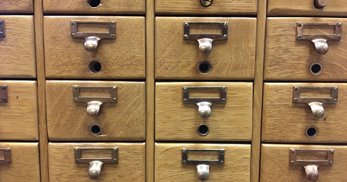 Rows of wooden library card catalog drawers with brass handles and label holders